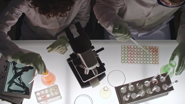 Top view of scientists in gloves mixing solutions and looking into microscope