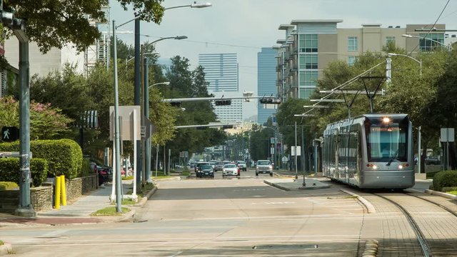 METRORail Light Rail Public Transportation Driving in the Streets of the Museum District in Houston TX with other Cars and Vehicles Past a Station on an Idyllic Day of Sunshine in Texas