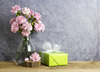 Pink carnation flowers in bottle and green gift box on old wood