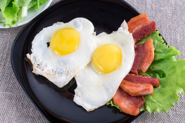 Top view on plate with fried eggs, bacon and lettuce close-up
