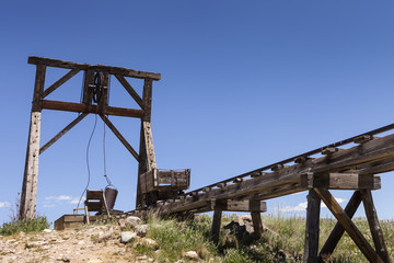 Old mining ore cart on trestle with head frame under blue sky.