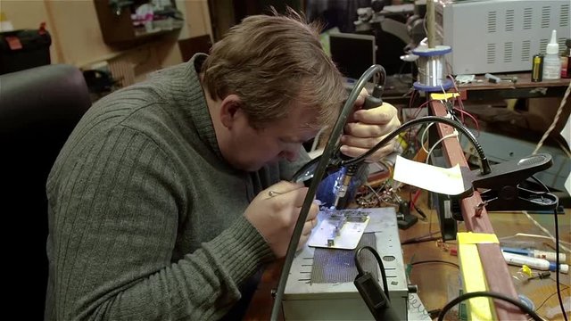 Engineer preparing motherboard of smartphone iphone to repair. White man in old workshop.