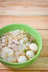 Noodles in green bowl on wood background.