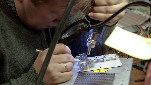 Engineer preparing motherboard of smartphone iphone to repair. White man in old workshop.