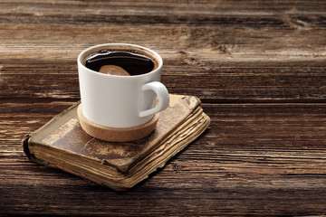 Old book and cup of coffee on wooden background