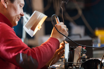 Man with safety glasses repairing motheboard with soldering iron