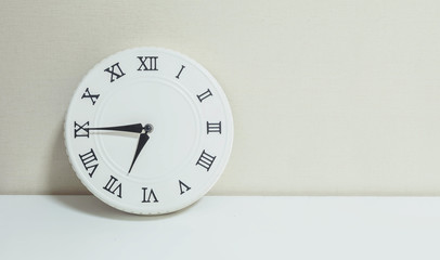 Closeup white clock for decorate show a quarter to seven or 6:45 a.m. on white wood desk and cream wallpaper textured background with copy space