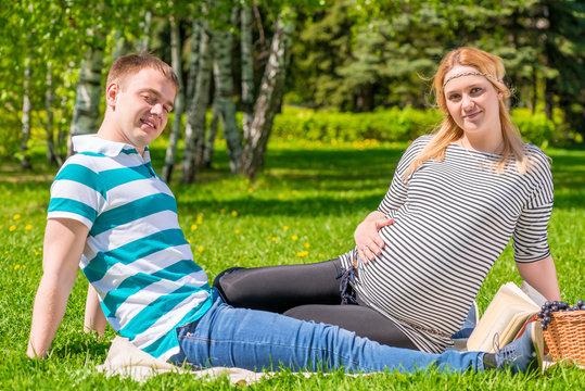 couple waiting for baby sitting in the park with a basket of fru