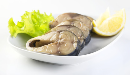 Pieces of mackerel and lemon on a white plate on a white background