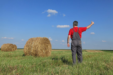 Naklejka na ściany i meble Farmer in hay field with bale gesturing, thumb up