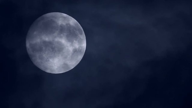 A bright full moon in darkness with clouds passing in front - beautiful moonscape real time view. This is a great clip for transitions.