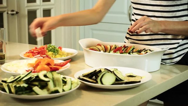 Cooking ratatouille. Female hands laying out the chopped vegetables in a baking dish. HD