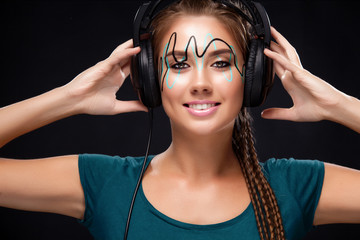 Modern young woman with art makeup enjoys listening to music in headphones. Positive emotions, leisure. Copy space.