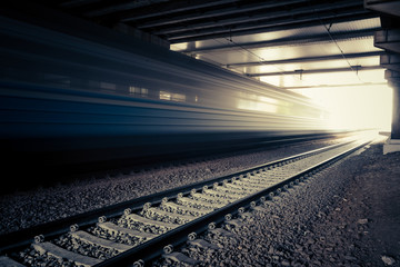 Obraz premium High speed passenger train on tracks moving out of tunnel with motion blur effect. Modern railway station.
