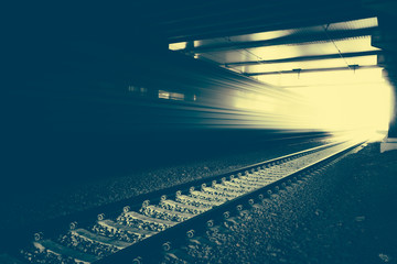 Obraz premium High speed passenger train on tracks moving out of tunnel with motion blur effect. Modern railway station.