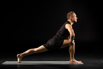 Man standing in yoga position in black sportwear on grey mat