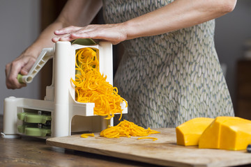 Woman preparing pumpkin noodles in spiral vegetable slicer