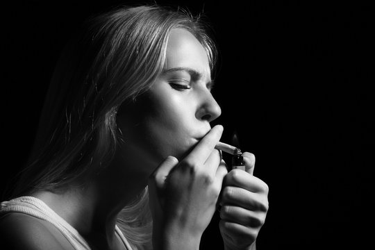 woman smoking joint of marijuana on black background, monochrome