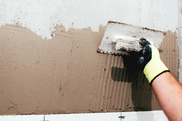 industrial close up of worker hand adding cement adhesive for ceramic tiles installation