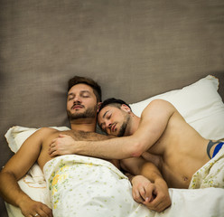 Handsome men lying on bed together sleeping embracing, shirtless