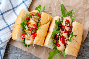 Mini hot dogs with vegetables on paper. Wooden background, top view.