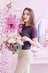 Beautiful young woman with long blonde hair, blue eyes, flowering cage, wearing t-shirt. Spring mood in pink rose tones