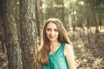 Outdoors portrait of beautiful young woman in casual green dress posing in summer garden. Smiles.