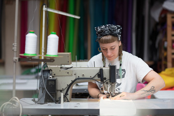 Young tattooed seamstress sewing in a factory environment