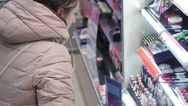 Woman chooses lipstick in cosmetics shop.