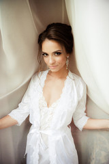 Beautiful happy bride in white silk lingerie in her bedroom in a morning 