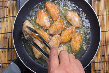 Chef frying chicken wings in pan