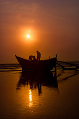 Fishermen preparing a boat to start fishing with sunset at background