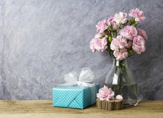 Pink carnation flowers in bottle and blue gift box on old wood