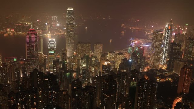Aerial view night time lapse of Victoria Harbour skyline from Lugard Road Lookout at Victoria Peak, highest mountain in Hong Kong Island. On backgrond, skyscrapers landmarks with their glowing lights.