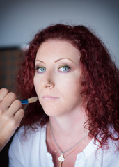 Red-haired lovely girl in a hairdressing salon makes  professional make-up