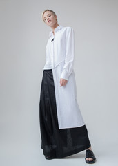 Stylish girl with blond short haircut in minimalist clothes. White linen long shirt and black long...