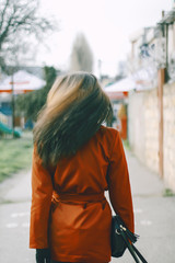 Obraz premium beautiful brunette girl standing with her back in a red trench. She turns her head, her hair fly