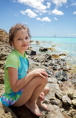 Fototapeta na wymiar Young girl sitting on the rocks at water's edge