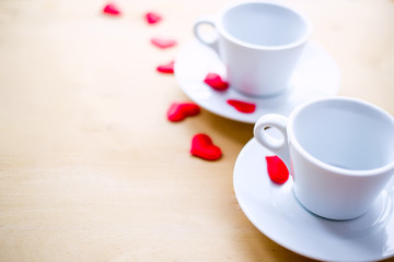 Couple cups decorated by red hearts on wooden table.