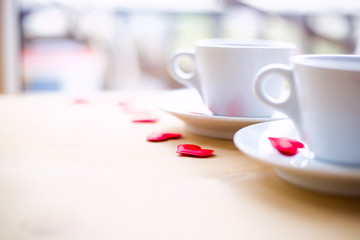 Couple cups decorated by red hearts on wooden table.