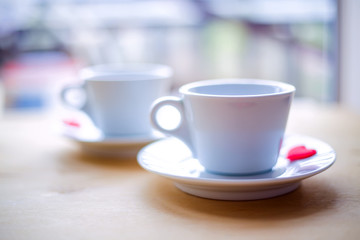 Couple cups decorated by red hearts on wooden table.