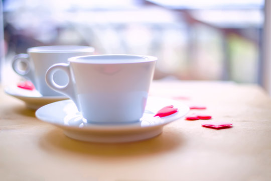 Couple cups decorated by red hearts on wooden table.