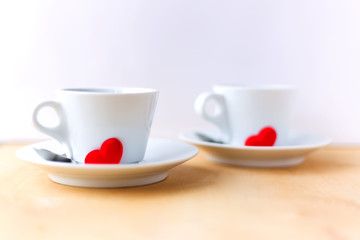 Couple cups decorated by red hearts on wooden table.