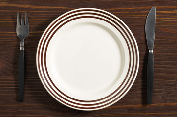 Empty plate with brown stripes and cutlery on brown wooden table, top view