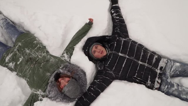 a girl and a guy lying on the snow in the winter