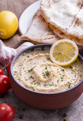 Humus in homemade bowl with lemon, tomatoes and chapation natural wooden desk.