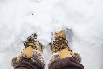 horizontal close up image of a pair of brown suede boots standing in the snow in the winter time with room for text.