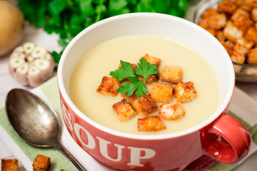 Homemade potato cream soup with croutons and parsley in red bowl on table