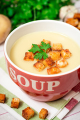 Homemade potato cream soup with croutons and parsley in red bowl on table