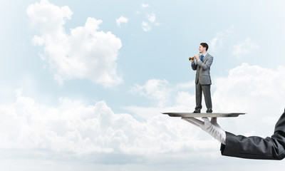 Obraz premium Businessman on metal tray playing fife against blue sky background